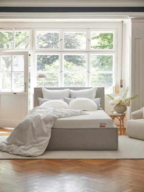 een grijs bed met matras, kussens en deken