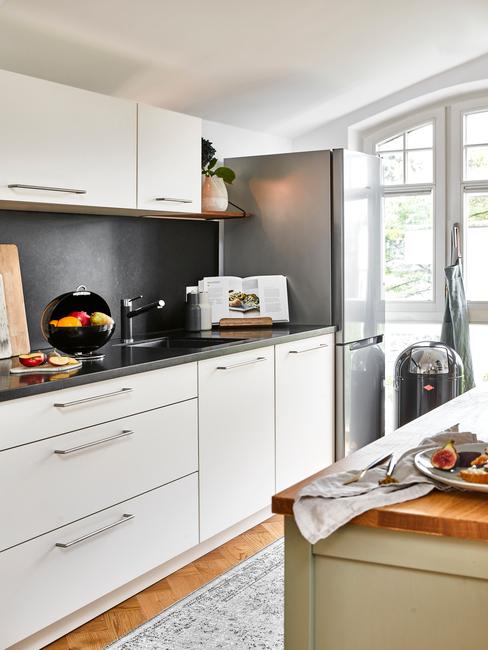 Kuchnia z szara ścianą, białymi frontami szafek oraz drewnianą wyspą kuchenną