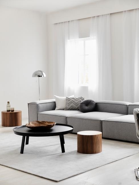 Szara, aksamitna sofa w salonie z czarnym i drewnianymi stolikami