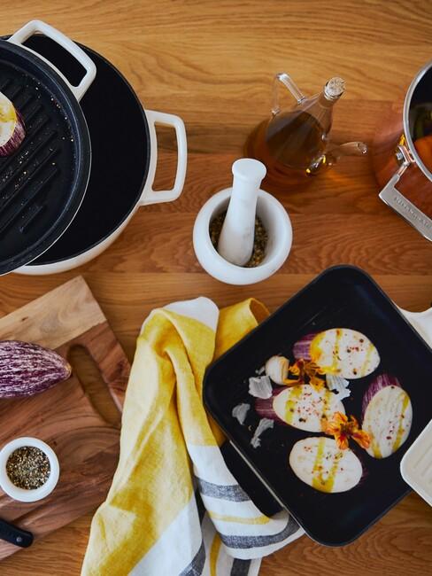 Kwadratowa patelnia grilowa z warzywamy na drewnianym blacie obok białego mozdzieża