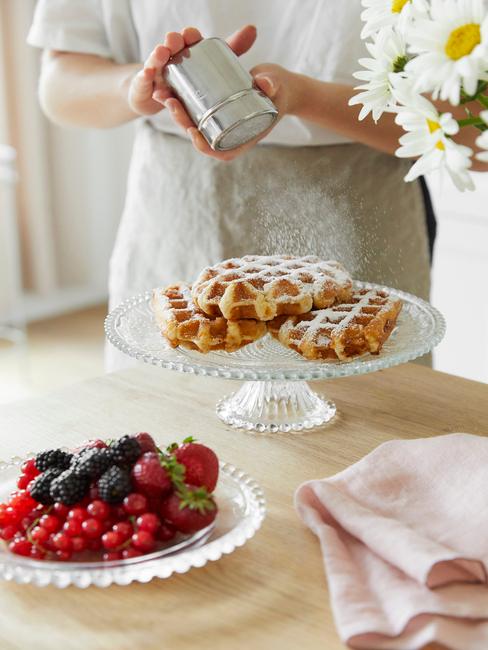 Gofry z Liege na białej paterze na drewnianym blacie oraz biały talerz z owocami