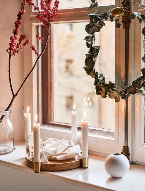Suszony wieniec z eukaliptusa na oknie. Na parapecie stoi wazon z ilexem i adwentowe świece.