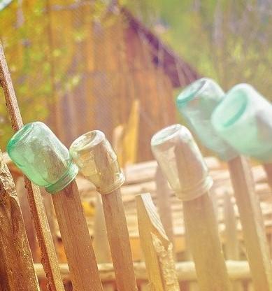 Drewniany płot na którym znajdują się szklane słoiki