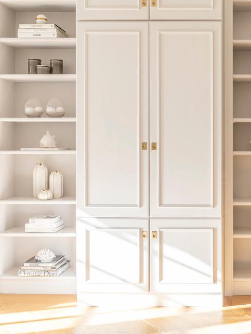 Biała szafa na ubrania, obok której stoi szafka z półkami i dekoracjami