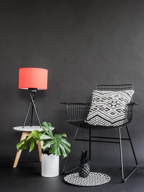 Wnętrze z czerną ścianą, foletem z biało-czarną poduszką, rośliną oraz czerwoną lampą