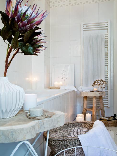 Fragment łazienki z wanną, drewnianym stolikiem oraz marmurowym stolikiem z kwiatami i świecami