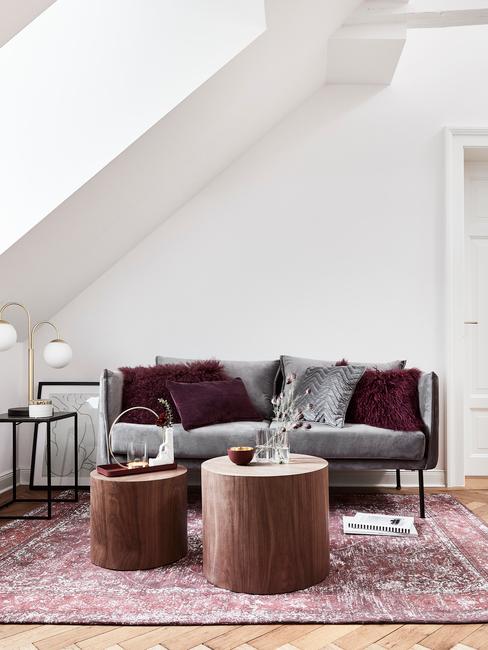 Przytulny salon na podda. Szara sofa oraz bordowy dywan.