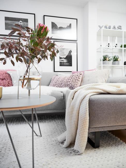 Szara sofa z jasnymi dodatkami. Na ścianie czarno-białe fotografie
