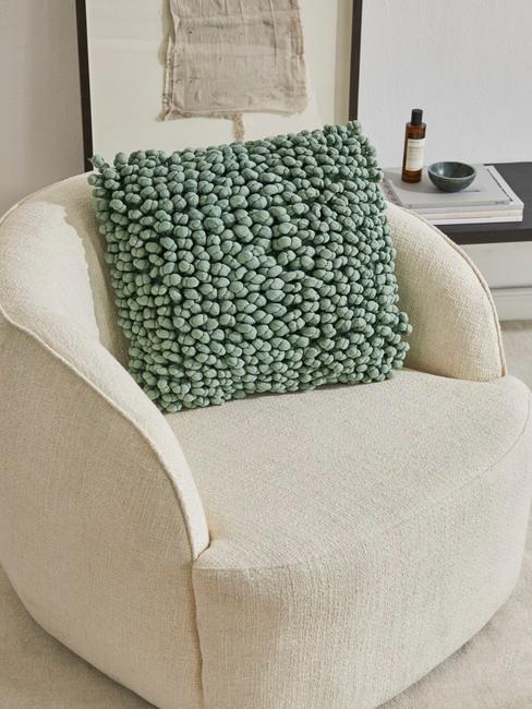 Poduszka w kolorze szałwiowej zieleni na beżowym fotelu