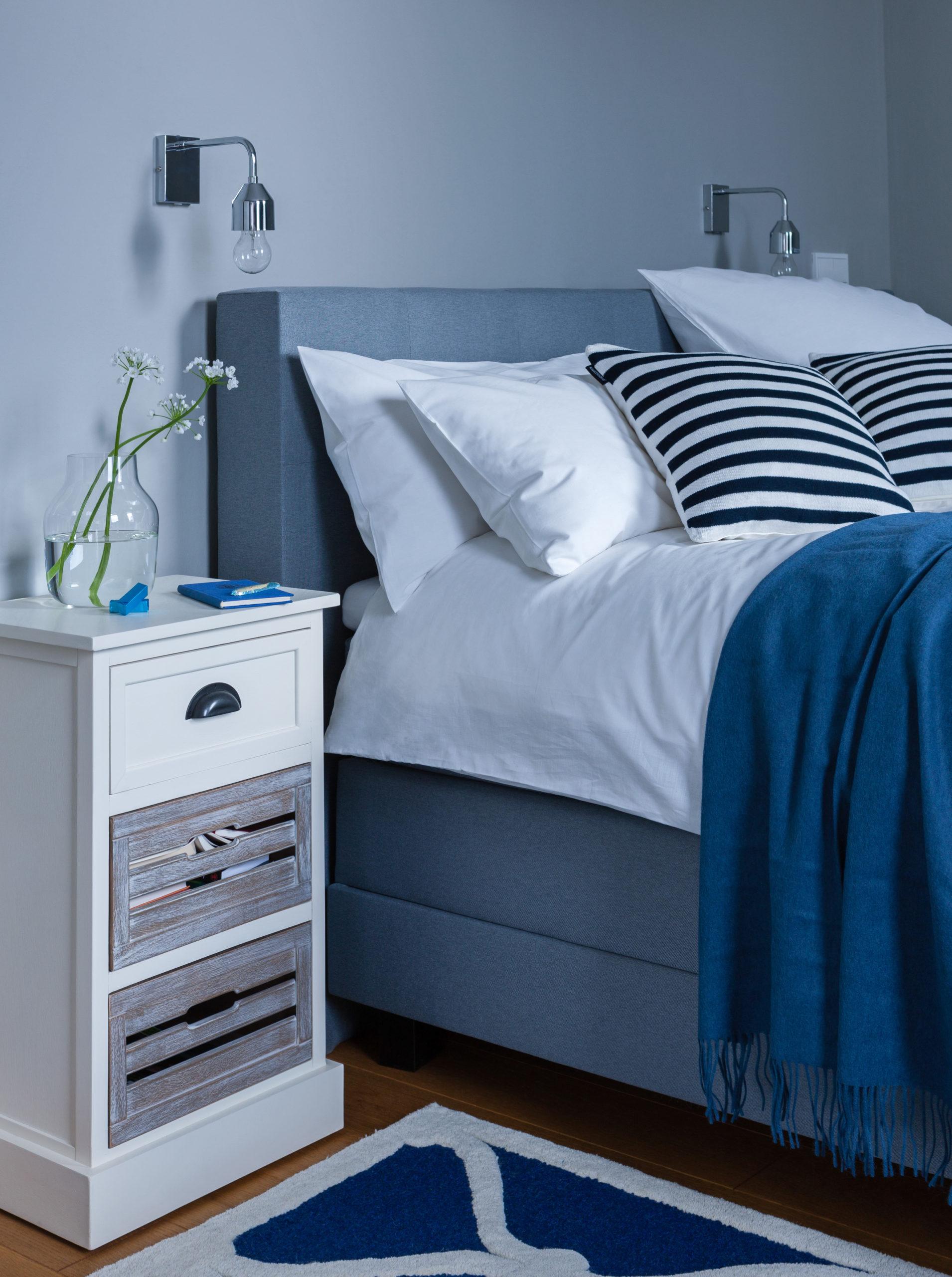 Granatowa sypialnia z podwójnym łożkie, białą szafką nocną oraz poduszkami dekoracyjnymi