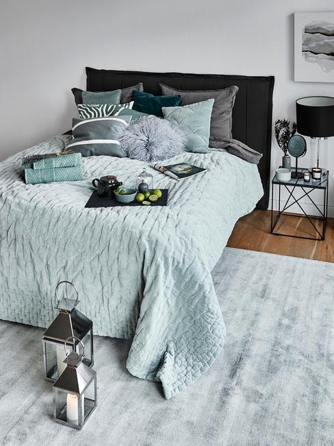 Sypialnia z turkusową pościelą, szarym dywanem oraz stolikiem nocnym