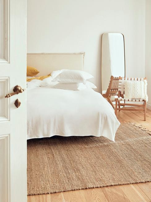 Beżowa sypialnia z łożkiem o białej pościeli oraz lustrze na ścianie