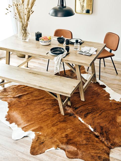 Drewniany stół przy którym stoją dwa skórzane krzesła oraz skórzany dywan