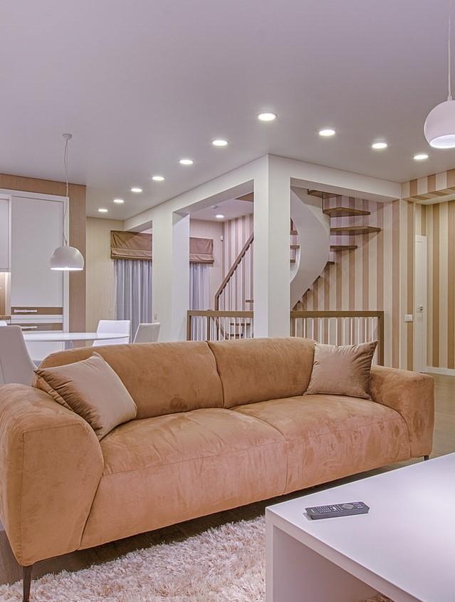 Salon z beżową kanapą, stolikiem kawowym oraz oświetlonymi schodami