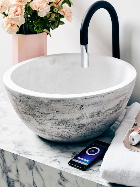 Marmurowy kran obok którego stoi różowy wazon z kwiatami