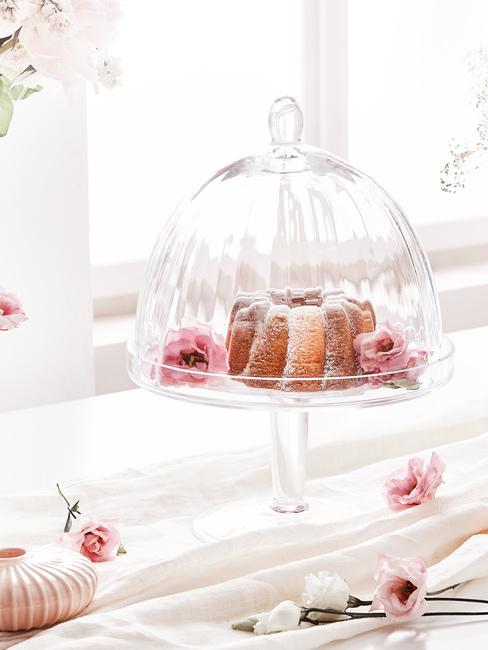 Szklana patera z ciastem oraz kwiatami ustawiona na parapecie przy oknie