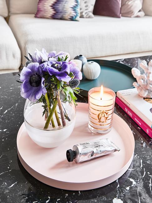 Stolik kawowy z czarnego marmuru. Na nim taca z wazonem i świecą