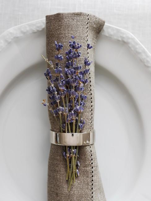 Lniana serwetka z suszonymi kwiatami lawendy z złotym pierścieniu ułożona na białym talerzu