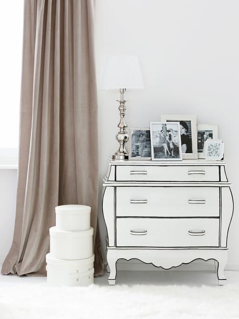 Biała komoda w stylu glam obok której stoją trzy okrągłe pudełka