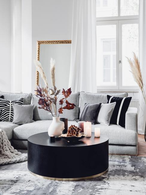 Salon w stylu glam z szarą, narożną kanapą oraz czarnym stolikiem kawowym