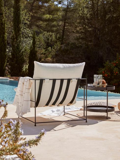 Leżak ustawiony przy basonie wraz z czarnym stolikiem pomocniczym