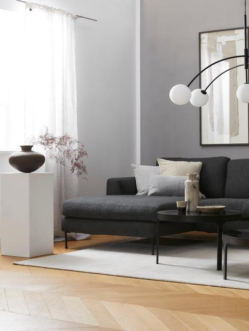 Salon z sofą w szarej barwie, białą kolumną z wazonem oraz stojąca lampą