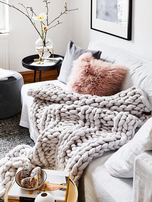 Zbliżenie na sofę z grubym, pledowym kocem oraz poduszkami w salonie w stylu skandynawskim