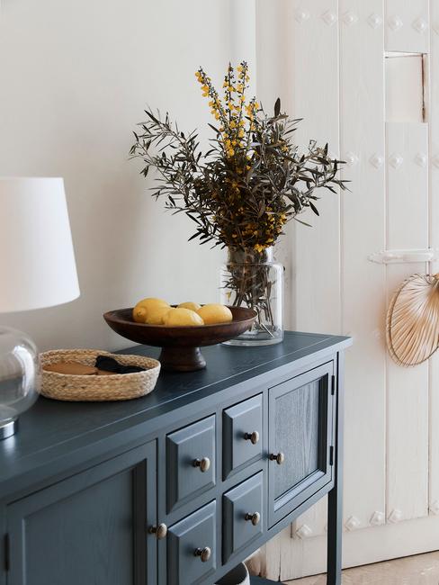 Fragment przedpokoju w białym kolorze i niebieską komodą z lampą oraz wazonem kwiatów