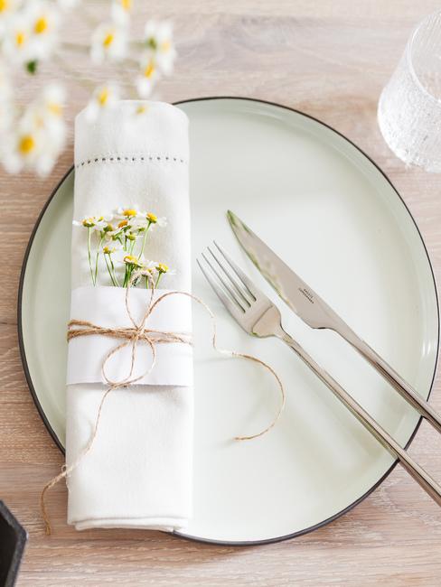 Fragment stołu z białym talerzem, srebrnymi sztućcami oraz rumiankiem