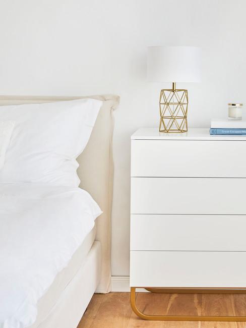 Wnętrze białej sypialni z łożkiem, prosta, białą komodą oraz minimalistycznymi dekoracjami