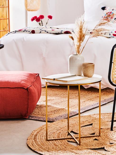 Fragment pomieszczenia z pufem, metalowym stolikiem kawowym na krótym znajduje się wazon oraz kubek z kamionki