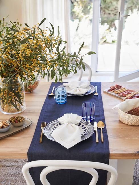 drewniany stół do jadalni z granatowym bieżnikiem i zastawą w bieli i wgranacie oraz ze złotymi sztućcami