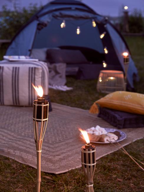 Zbliżenie na niebieski namiot udekorowany girlanda świetlną weraz z dywanem, pufem oraz poduszkami