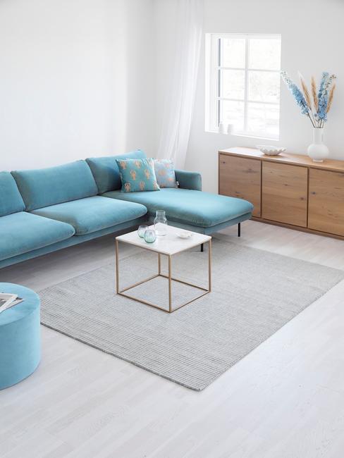 Jasny salon z trukusową, aksamitną sofa, marmurowym stolikiem oraz drewnianą komodą
