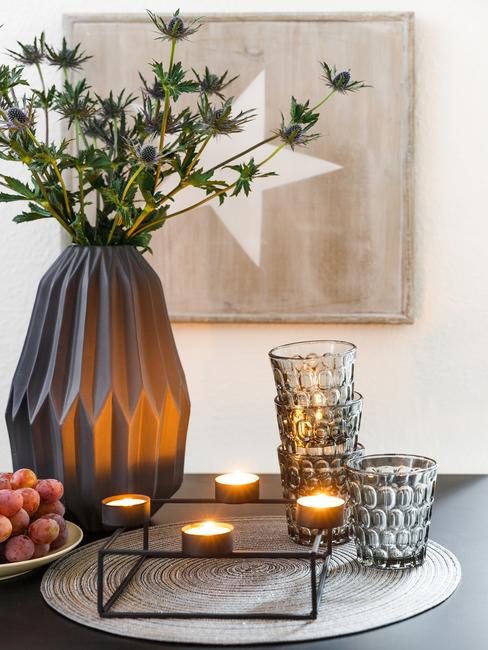 Zbliżenie na ceramiczny wazon z kwiatami, świeczki z świeczniki oraz szklanki z przydymionego szkła