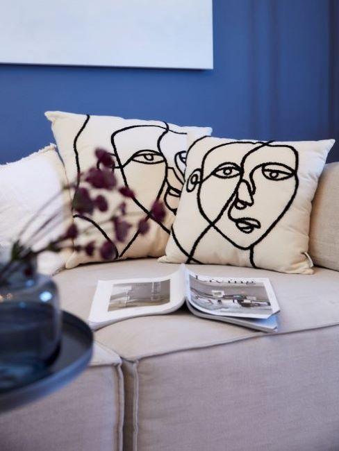 Salon z niebieską ściną, białą kanapą oraz dwoma poduszkami dekoracyjnymi