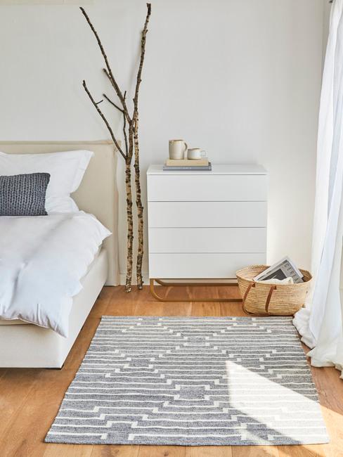 Minimalistyczna sypialnia w stylu scandi z białą komodą, dywanem oraz galęziami obok łóżka