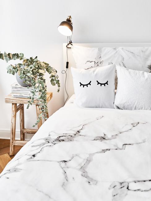 Zbliżenie na łóżko z pościelą ze wzorem sylizowany na marmur oraz roślinę w donicznce