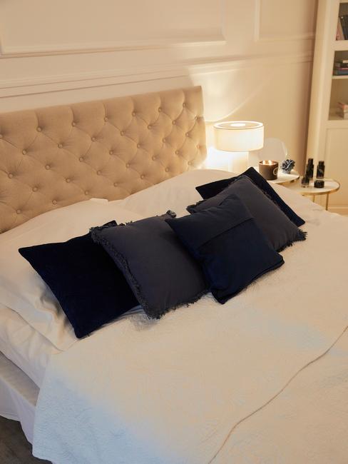 Sypialnia ze złotymi ścianami, łożkiem o pikowanym zagłówku oraz niebieskich poduszkach