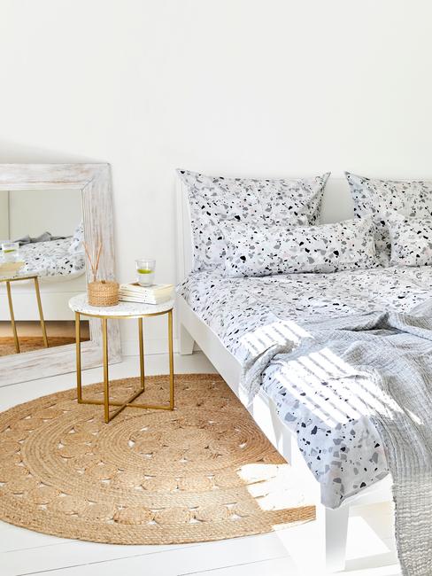 Sypialnia z łożkiem z niebiesko - białą pościelą, jutowym, okrągłym dywanem oraz stoliczkiem