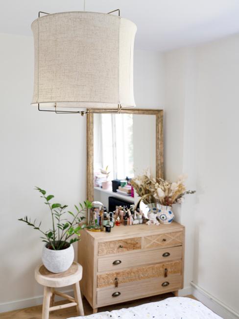 Zbliżenie na drewnianą komodę w pomieszczeniu z lustrem, kosmetykami oraz wazonem