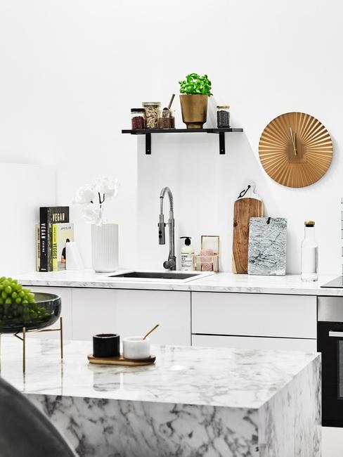 Biała kuchnia z marmurową wypsą, białymi meblami oraz akcesoriami kuchennymi