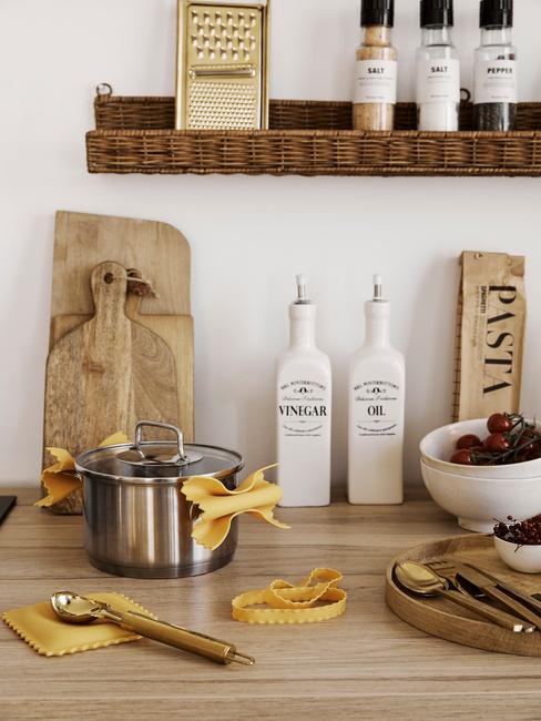 Zbliżenie na drewniany blat z deskami, garnkiem oraz pojemnikami na oliwę oraz wiklinową półką