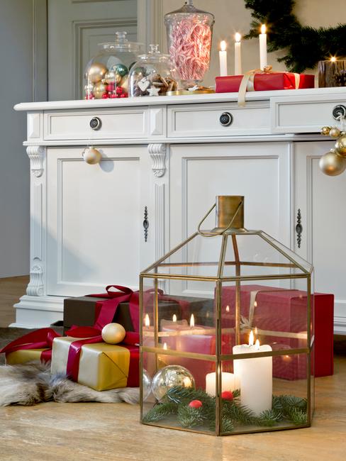 Biała komodaw przedpokoju ze świeczkami i dekoracjami oraz szklana latarenka na podłodze