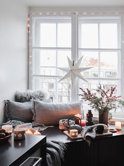 Wykusz ozdobiony poduszkami, świeczkami, czajnikiem i kubeczkami oraz gwiazdą powiedzoną na oknie