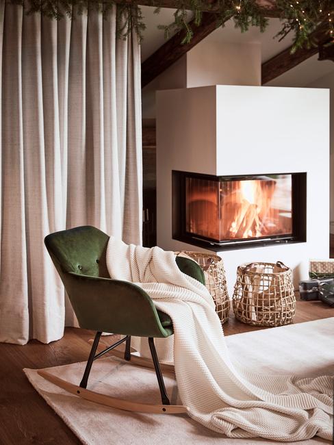 Fragment salonu z kominkiem, w którym znajduje się zielony fotel z białym kocem