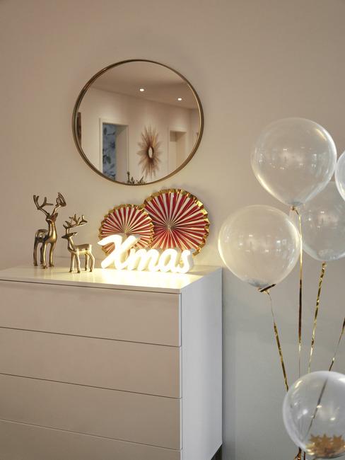 Biała komoda z dekoracjami świątecznymi, neonowym światłem nad którą wisi lustro