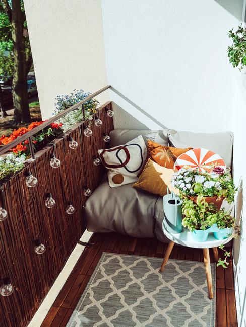 Balkon z dywanem zewnętrznym, fotelem z poduszkami i stoliczkiem z roślinami w doniczkach