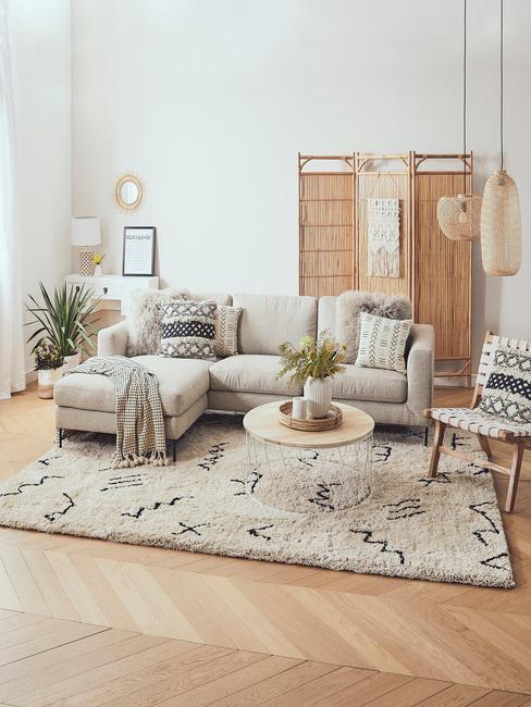 Salon w stylu boho z narożną, beżową sofą, dywanem, stolikiem kawowym, parawanem i roślinami w doniczkach