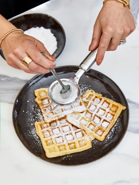 Trzy gofry brukselskie posypane cukrem pudrem na czarnym talerzu